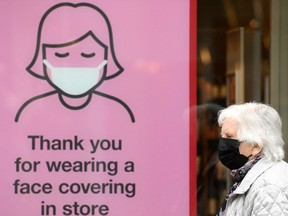 A member of the public wearing a face mask passes a sign reminding shoppers to wear face coverings inside a store.