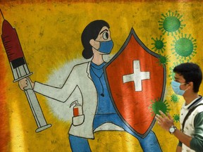 A student walks past a wall mural depicting a health worker wearing a facemask while holding a vaccine and a shield to spread awareness about the Covid-19.