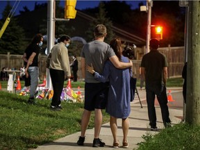 People and members of the media are seen Monday evening at a makeshift memorial at the fatal crime scene where the driver of a pickup truck jumped the curb and ran over a Muslim family in what police say was a deliberately targeted anti-Islamic hate crime, in London, Ont.