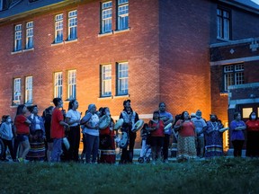 Kamloops residents and First Nations people gather to listen to drummers and singers at a memorial in front of the former Kamloops Indian Residential School after the remains of 215 children, some as young as three years old, were located at the site recently.