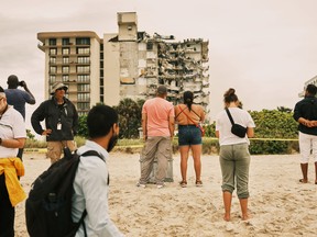 People gather on the beach to see the rubble from the Champlain Towers South building after the residential building partially collapsed in Surfside, Fla.