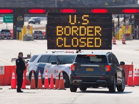 U.S. Customs officers speak with people in a car beside a sign saying that the U.S. border is closed, at a border crossing in Lansdowne, Ont., on March 22.