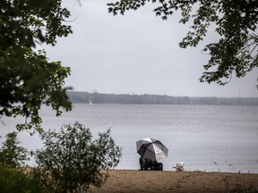 Files: A man sits under an umbrella fishing in the Ottawa River by Petrie Island Beach, Saturday, June 26, 2021.
