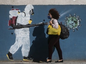 FILE: A woman wearing a mask walks past a wall with a graffiti depicting a cleaner in protective gear spraying viruses with the face of President Jair Bolsonaro in Estacio neighbourhood amidst the coronavirus (COVID-19) pandemic on June 8, 2020 in Rio de Janeiro, Brazil.