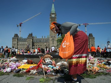 Jacqueline Shigwadja, from Wikwemikong First Nation near Manitoulin Island, lays cedar around the display of toys and shoes representing the children found buried at residential schools on Parliament Hill on Saturday.