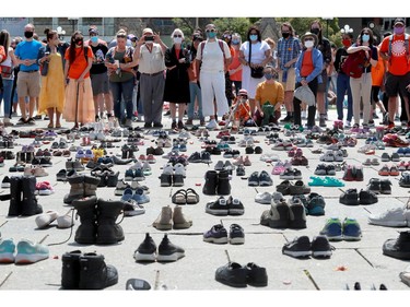 Standing behind the hundreds of little shoes that represented the original 215 children found buried at a residential school, people listen to the speakers on Parliament Hill before the march in downtown Ottawa on Saturday.