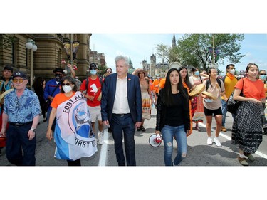 Hundreds joined MPs Charlie Angus (centre) and Mumilaaq Qaqqaq and Indigenous elders for Saturday's march to demand an independent investigation into the deaths at residential schools.