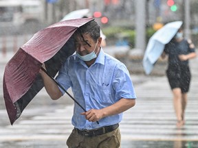 People cross the street in the wind and rain along in Ningbo on July 25, 2021, as Typhoon In-Fa lashes the eastern coast of China.