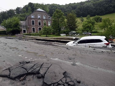 A wrecked car lies half buried besides a damaged road in an area destroyed by recent flood waters in Trooz on 16 July 2021.