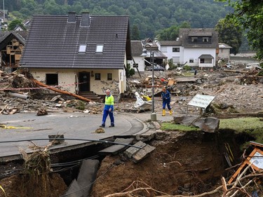 Two men walk on a partially slipped road amid destroyed houses after the floods caused major damage in Schuld near Bad Neuenahr-Ahrweiler, western Germany, on July 16, 2021.
