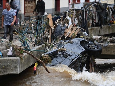 A man walks past a car stuck in the channel, on July 16, 2021, in the pedestrian area of Bad Muenstereifel, western Germany, after heavy rain hit parts of the country, causing widespread flooding.