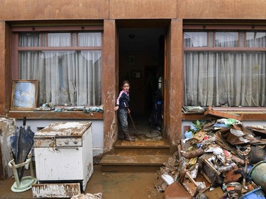 A young resident stands in the doorway of a home as damaged household goods are brought outside during the clean-up  following heavy rains and floods in the town of Rochefort on July 17, 2021.