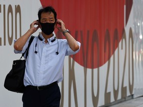 A man wearing a protective mask, amid the coronavirus disease (COVID-19) outbreak, walks past a sign of Tokyo 2020 Olympic Games in Tokyo, Japan.