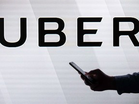 Files: A man checks his smartphone while standing against an illuminated screen bearing the Uber logo in London on June 26, 2018.