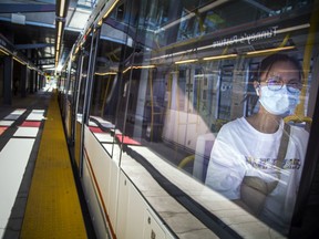 A young woman sits on a train wearing a face mask.