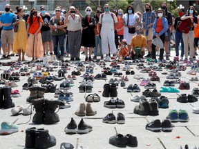 Standing behind the hundreds of little shoes that represented the original 215 children found buried at a residential school, people listen to the speakers on Parliament Hill before a march in downtown Ottawa this past summer.