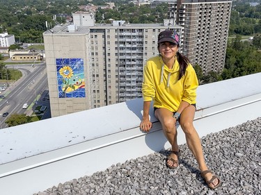 Artist Claudia Salguero poses for a photo in a neighbouring building with The Wisdom Mural shown in teh background.