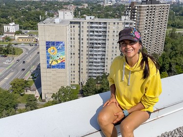 Artist Claudia Salguero poses for a photo in a neighbouring building with The Wisdom Mural shown in teh background.