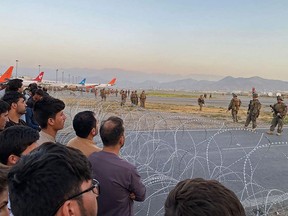 Afghans (L) crowd at the airport as US soldiers stand guard in Kabul on August 16, 2021.