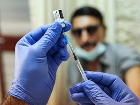 A man looks on as a medic prepares a dose of the Pfizer-BioNTech COVID-19 coronavirus vaccine.