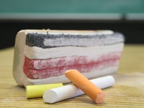 File - Chalk and an eraser sit on a desk in an empty classroom.