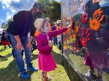 3 year old Èloïse Barrette, with her father Christian, places her painted hand print on an art installation to recognize Indigenous voices in Confederation Park on the inaugural National Day for Truth and Reconciliation.