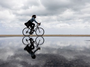 FILE: A woman wearing a face mask rides her bike past a rain puddle.