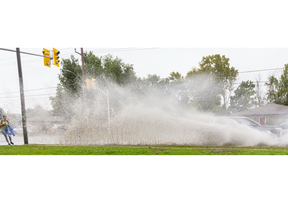 Mikkayla Longland flinches as she's sprayed by a car going through a large puddle on Sarnia Road at the base of the Brescia Hill in London. Longland was walking home from classes at Western University. Heavy rains are expected to continue to Thursday.