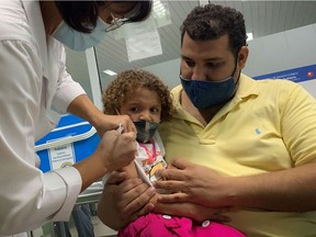 (FILES) In this file photo taken on August 24, 2021 Pedro Montano holds his daughter Roxana Montano, 3, as she is inoculated against COVID-19 with Cuban vaccine Soberana Plus/