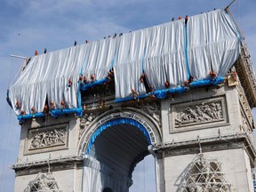 Workers unravel silver blue fabric, part of the process of wrapping L'Arc de Triomphe in Paris on September 12, 2021, designed by the late artist Christo. - Work has begun on wrapping the Arc de Triomphe in Paris in silvery-blue fabric as a posthumous tribute to the artist Christo, who had dreamt of the project for decades.