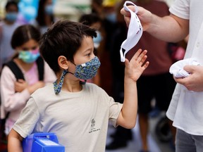 A school staff member hands a face mask to a boy.