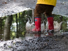 A young child wearing rain boots jumps into a puddle.