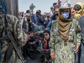 Taliban members stand next to people rushing to pass to Pakistan from the Afghanistan border in Spin Boldak on Sept. 25, 2021.