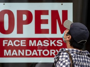 A pedestrian wearing a mask reads signage stating “Open Face Masks Mandatory” in Toronto during the pandemic.
