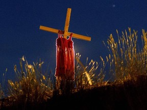 (FILES) In this file photo taken on June 06, 2021, a child's dress is hung on a cross on the side of Highway 5, near the former Kamloops Indian Residential School, where the remains of 215 children were discovered buried near the facility.