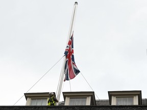 A worker lowers the British Union flag on the roof of 10 Downing Street, London, after MP David Amess was stabbed during constituency surgery,