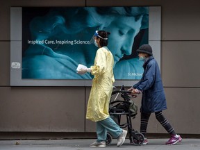 A health care worker guides a woman wearing a mask outside of St. Michaels Hospital in Toronto during the COVID-19 pandemic.