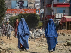 A banner with a picture of late Afghan commander Ahmad Shah Massoud is installed next to residential buildings as burqa-clad Afghan women walk along an under-construction road in Kabul on September 8, 2021.