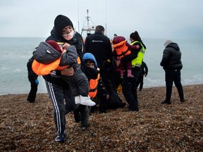 A migrant carries her children after being helped ashore from a RNLI (Royal National Lifeboat Institution) lifeboat at a beach in Dungeness, on the south-east coast of England, on November 24, 2021, after being rescued while crossing the English Channel. -