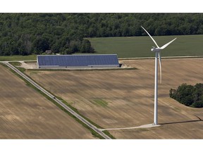 A wind turbine stands near a farm building with solar panels on the roof in Norfolk County near Simcoe, Ont.