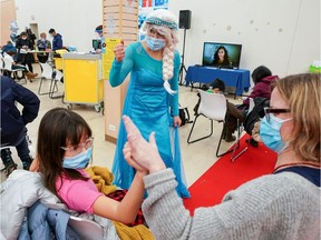 A woman dressed as Elsa cheers on Kate Rhodes and her mom Emma Rhodes as health workers with Humber River Hospital at a vaccination clinic for children aged 5 to 11, in Toronto. Ottawa's clinics for children begin Friday.