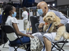 Files: Zootherapist Sylvain Gonthier and dog Bidule comforts a young girl  she waits to receive a COVID-19 vaccine at a clinic in Montreal, Thursday, Aug. 26, 2021.