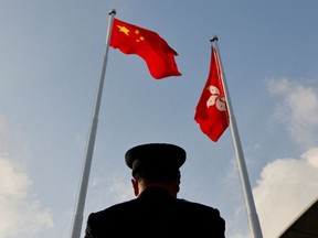 A police officer stands guard below China and Hong Kong flags during a flag raising ceremony, a week ahead of the Legislative Council election in Hong Kong, China, Dec. 12, 2021.