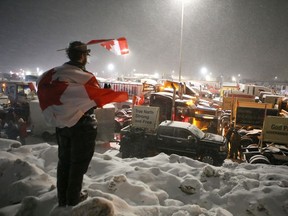 Erin O'Brien of Kingston stands on a snow bank to welcome the trucks participating in the convoy as they arrive in town Thursday night.  The convoy is on its way to Ottawa for a rally on Parliament Hill on Saturday.