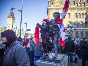 A protester stands on the Terry Fox statue that was outfitted with Canada flags and earlier had signage stuck to it.