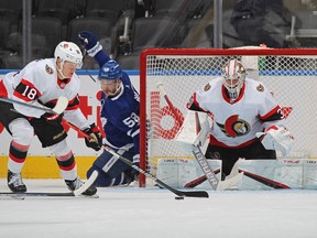Tim Stutzle (18) of the Ottawa Senators clears a puck for teammate Matt Murray (30) against Michael Bunting (58) of the Toronto Maple Leafs during an NHL game at Scotiabank Arena on Jan. 1, 2022 in Toronto.