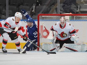 Tim Stutzle (left) of the Ottawa Senators clears a puck for teammate Matt Murray against Michael Bunting of the Toronto Maple Leafs during an NHL game at Scotiabank Arena on Jan. 1, 2022 in Toronto, Ontario, Canada.