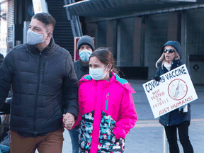 People walk past an anti-vaccine protester as they walk towards a children's COVID-19 vaccine clinic in Toronto.