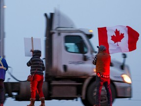 Supporters of the "freedom convoy" of truckers wait for the convoy along the Trans-Canada Highway east of Calgary on Monday, January 24, 2022. The truckers are driving across Canada to Ottawa to protest the federal government's COVID-19 vaccine mandate for cross-border truckers.