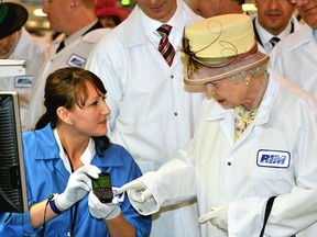 Queen Elizabeth II, wearing a white protective coat (R), is shown a new product, at the final testing before packaging test area during her tour of the RIM (Research In Motion) factory that produces the Blackberry mobile communications handset, on July 5, 2010 in Waterloo, Canada.